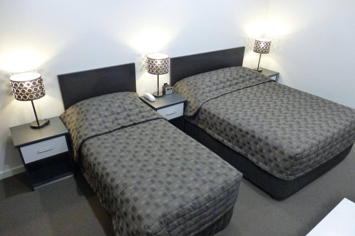 A hotel room with two beds, each with a nightstand and a lamp.