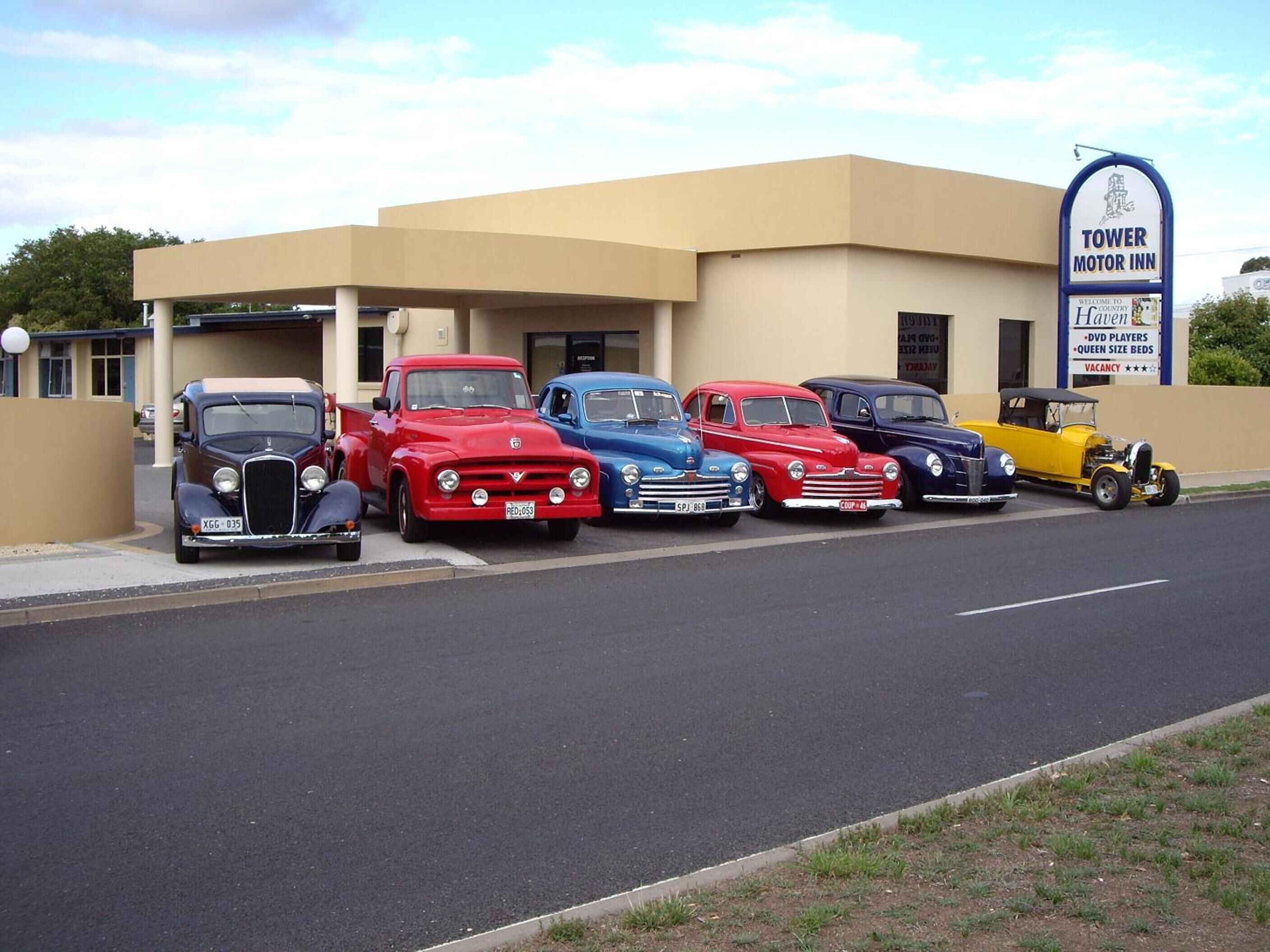 A row of vintage cars parked in front of a building with a sign reading "Tower Motor Inn".
