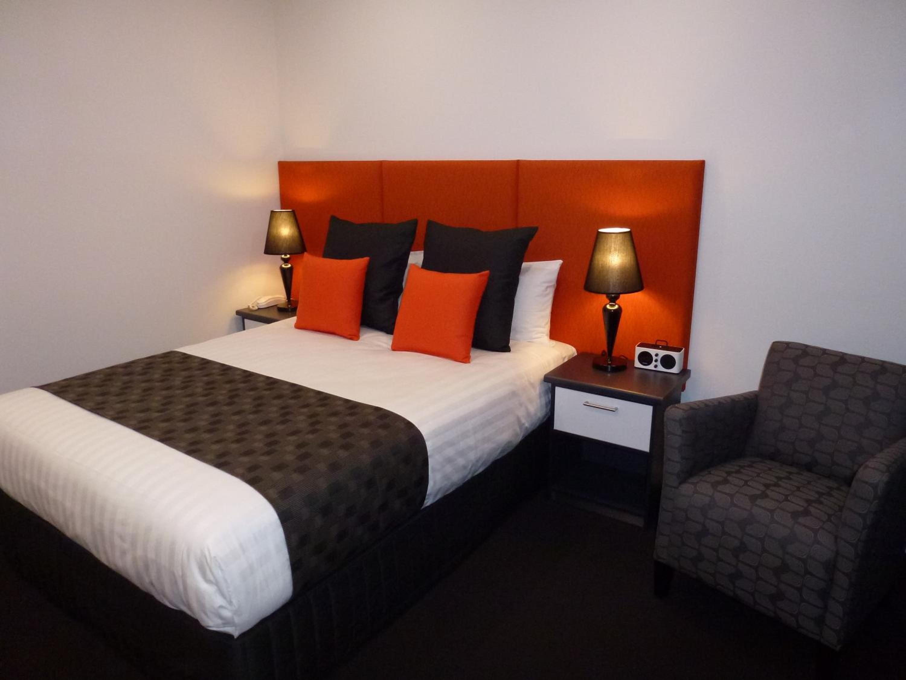 A hotel room with a bed, two bedside tables, a chair, and a headboard.