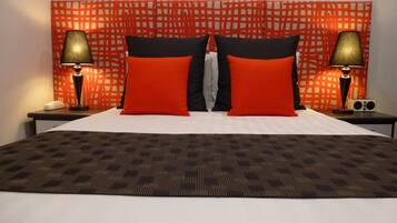 Habitación de hotel con una cama grande, dos almohadas rojas y negras, una colcha estampada y dos mesitas de noche con lámparas y un radio.