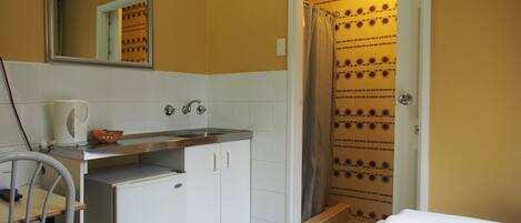 A compact hotel room with a kitchenette, a shower, and a bed.