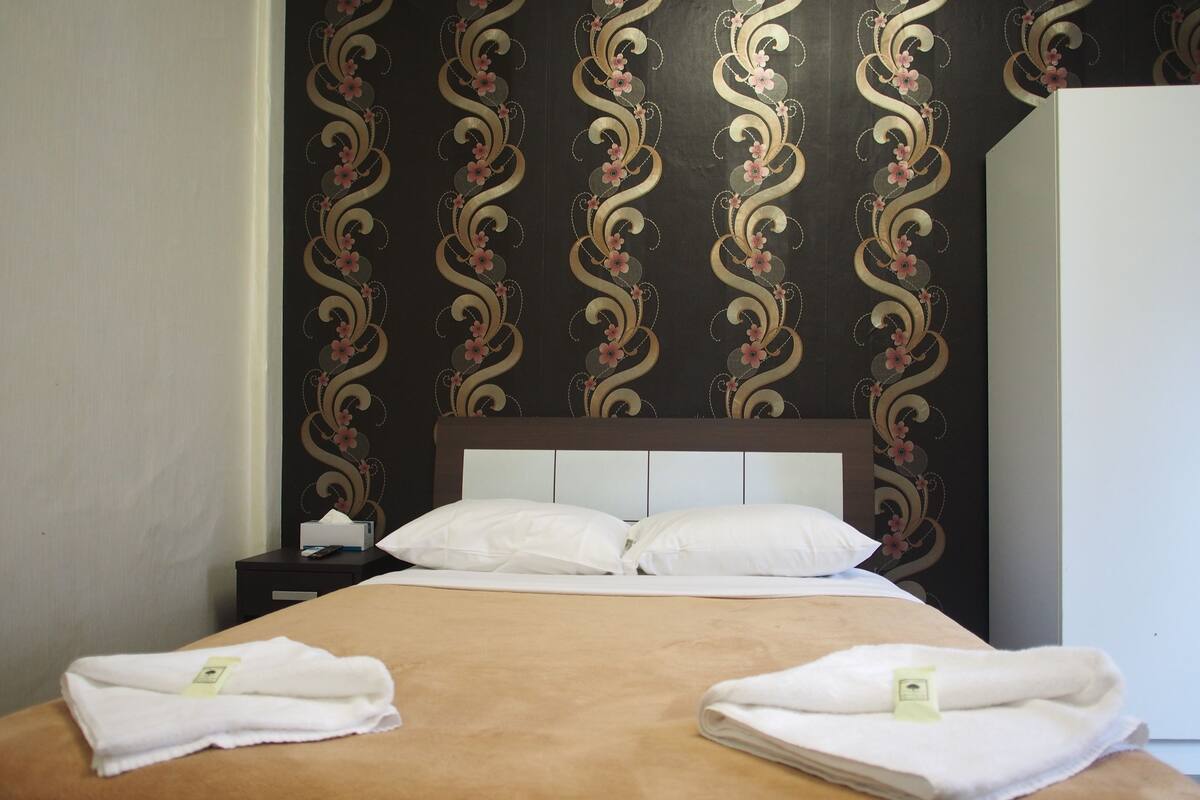 A neatly made bed with white linens and two folded towels on the bed.