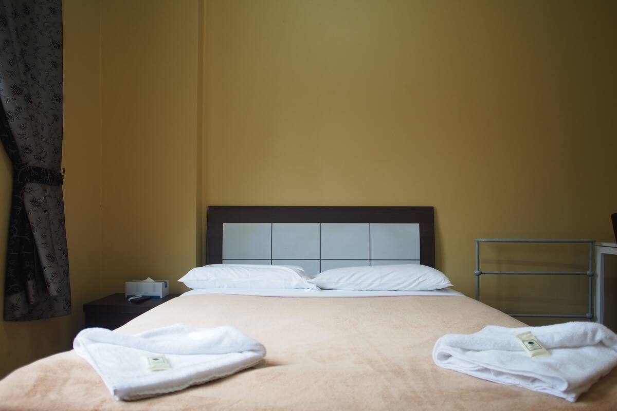 A hotel room with a bed, a nightstand, a window, and a curtain.