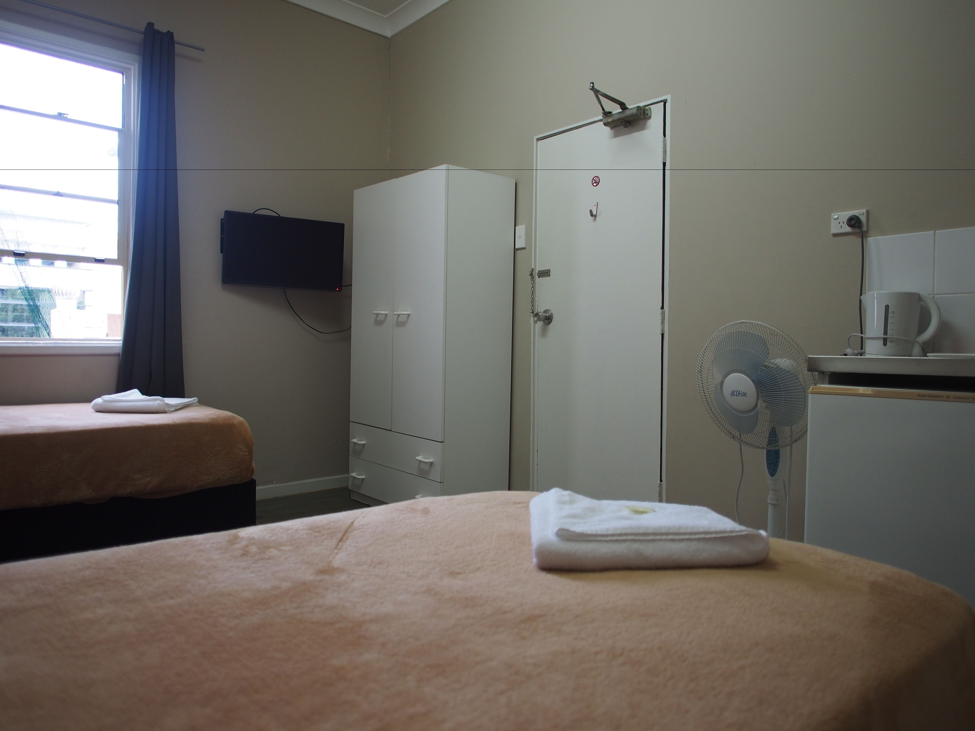 A hotel room with two beds, a wardrobe, a television, a fan, and a coffee maker.