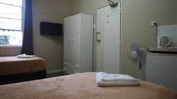 A hotel room with two beds, a wardrobe, a television, a fan, and a coffee maker.