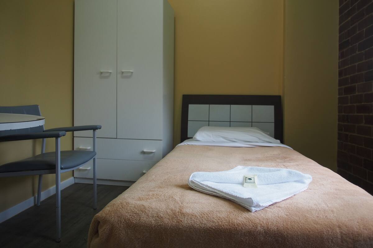 A small, single-bed room with a wooden headboard, a desk with a chair, and a wardrobe.
