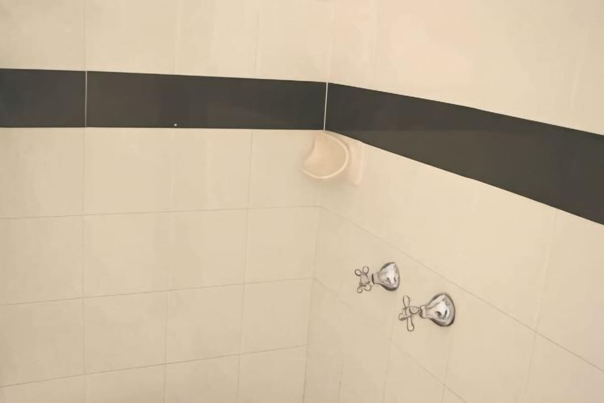 Un baño con azulejos blancos, una franja negra y un dispensador de jabón para manos.