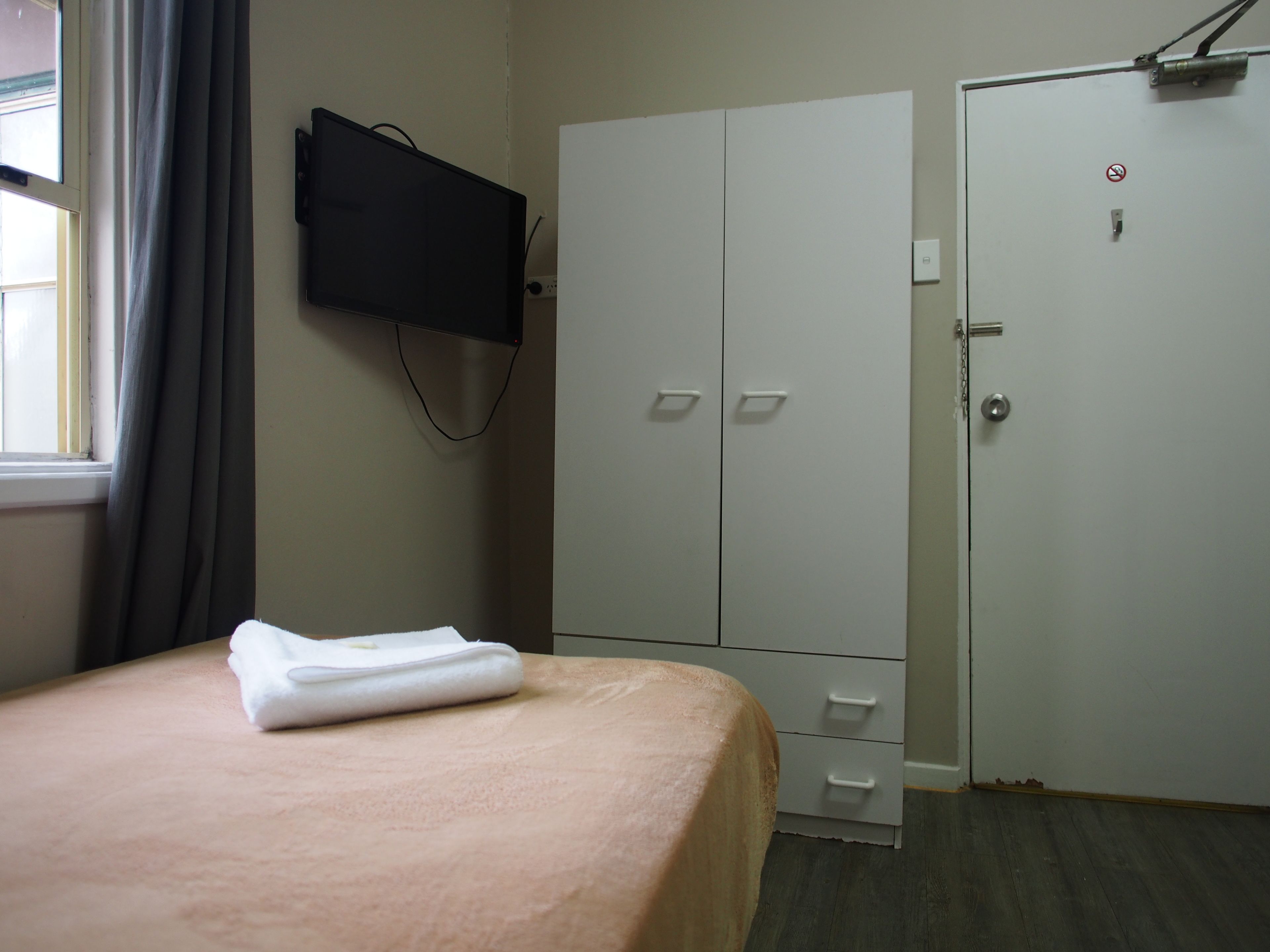 A bedroom with a bed, a wardrobe, a television mounted on the wall, and a door with a lock.