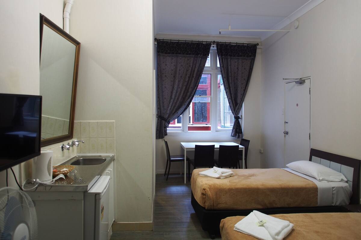 A hotel room with a bed, a desk, a chair, a TV, and a sink.