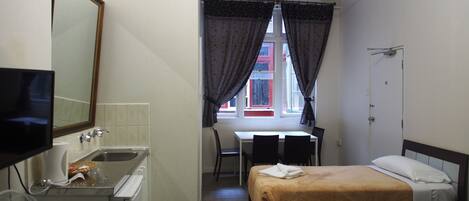 Habitación de hotel con cama, escritorio, silla, televisor y lavamanos.