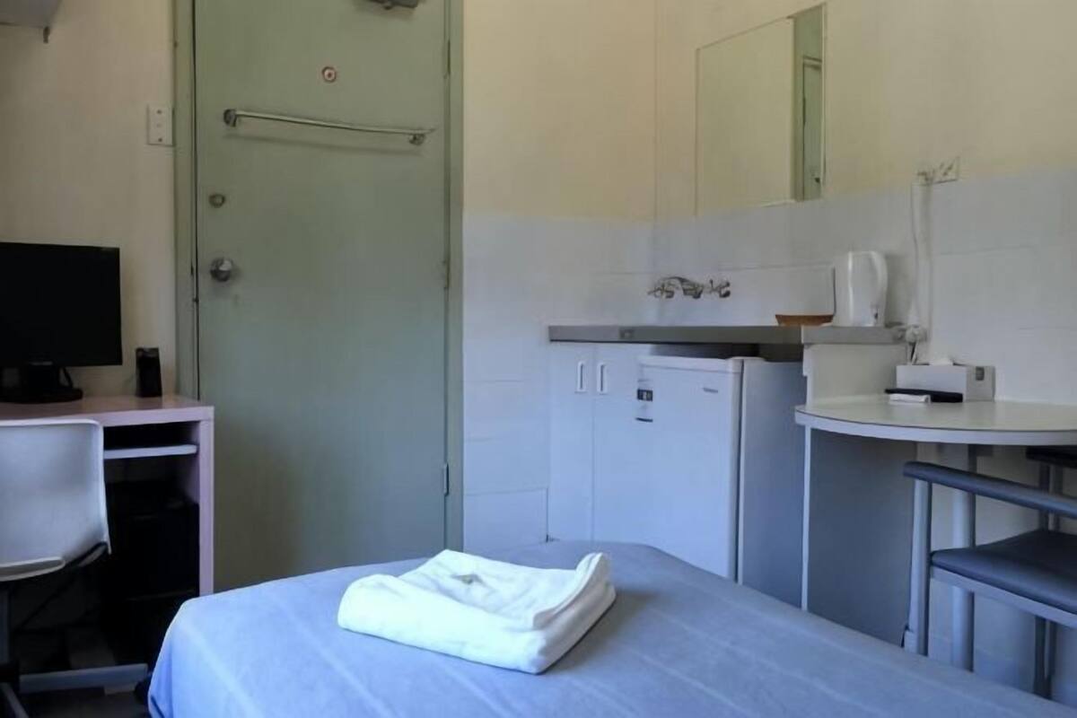 A hotel room with a bed, a desk with a computer, a small refrigerator, a sink, and a mirror.