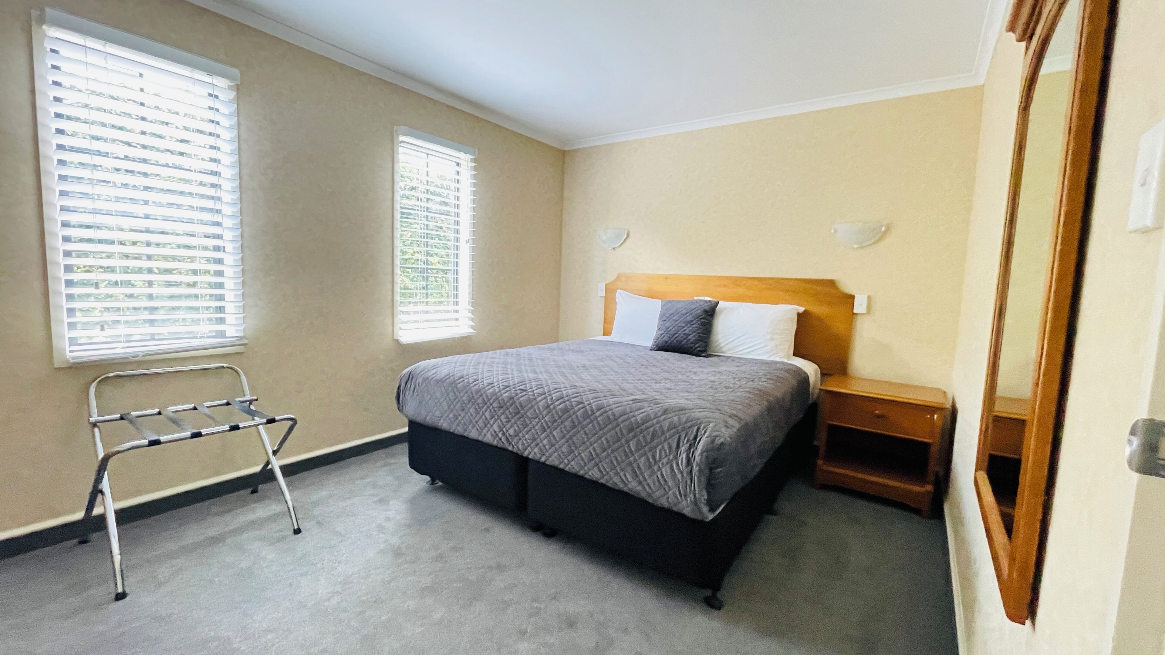 A bedroom with a bed, two windows, a nightstand, and a wheelchair.