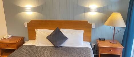 A neatly made bed with a quilted cover, two bedside tables, a lamp, and a wall-mounted light fixture.