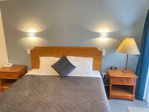 A neatly made bed with a quilted cover, two bedside tables, a lamp, and a wall-mounted light fixture.