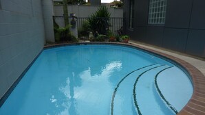 A rectangular swimming pool with a brick edge, surrounded by a low brick wall and a metal fence. - City Suites Tauranga (Tauranga)