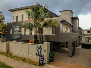 A modern building with a sign indicating it is a city suites hotel offering amenities like a swimming pool, spa baths, conference rooms, and underground parking.