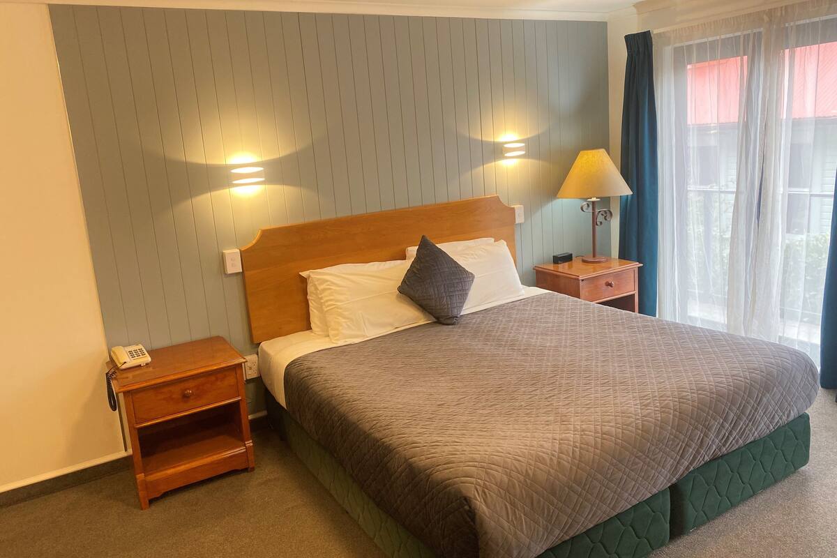 Habitación de hotel con una cama grande, una mesita de noche de madera, una lámpara de noche y un aplique de pared.