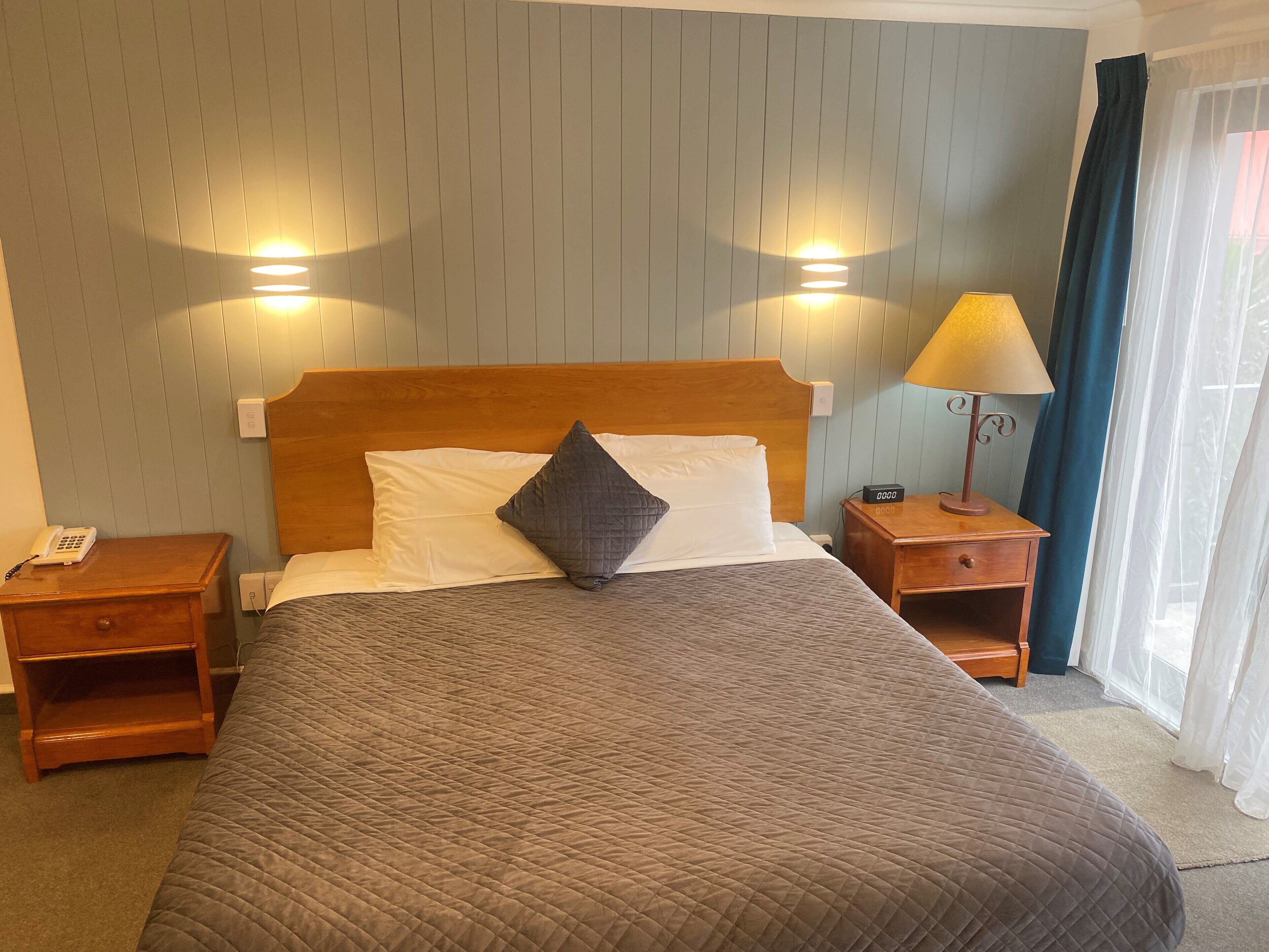 A hotel room with a wooden bed, two bedside tables, a lamp, and a phone on the left side.