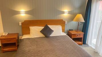 A hotel room with a wooden bed, two bedside tables, a lamp, and a phone on the left side.