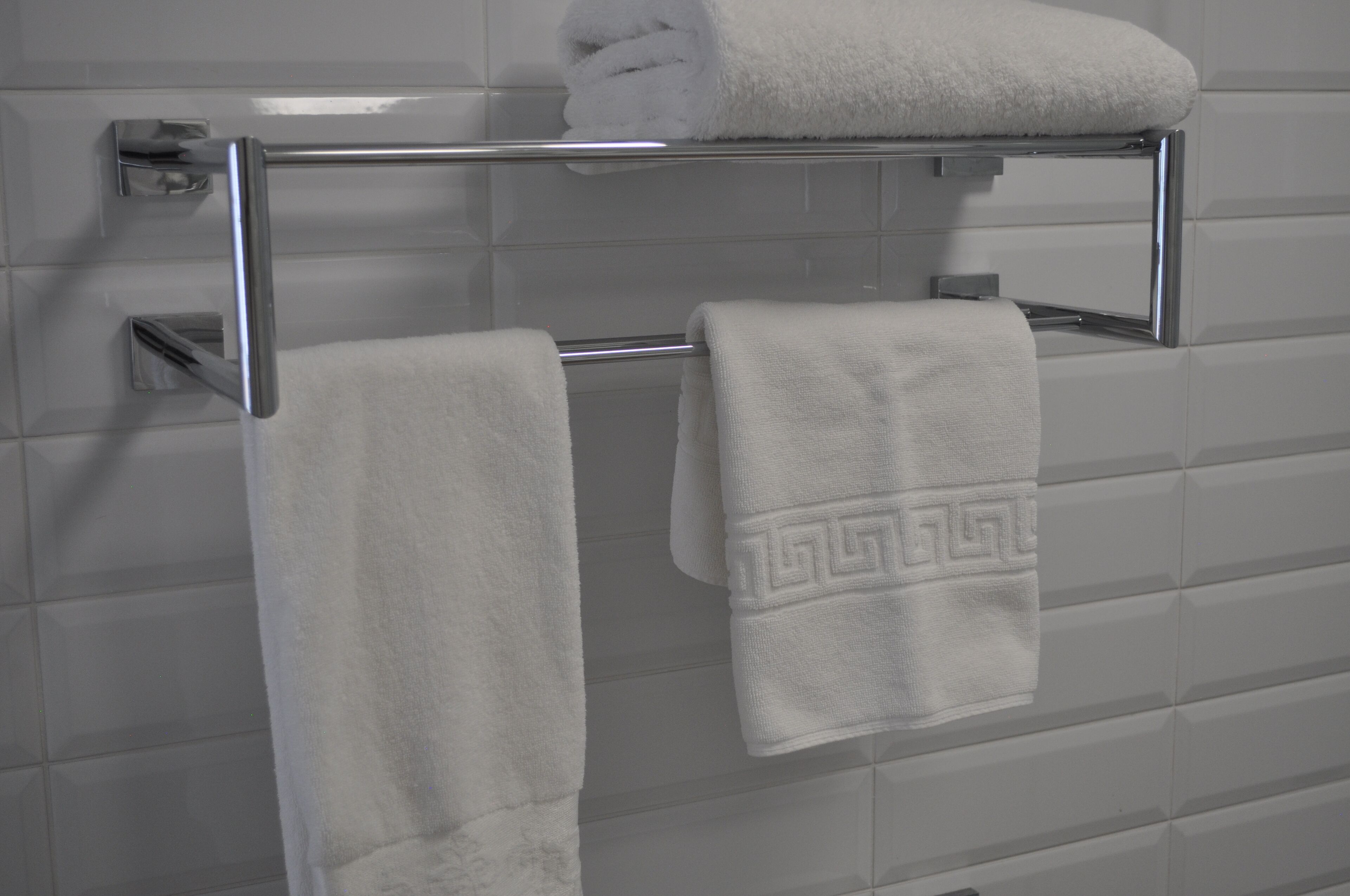 Une salle de bain avec un porte-serviettes chromé sur lequel sont posées deux serviettes blanches, l’une unie et l’autre à motifs géométriques.