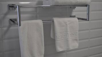 A bathroom with a chrome towel rack holding two white towels, one plain and one with a geometric pattern.