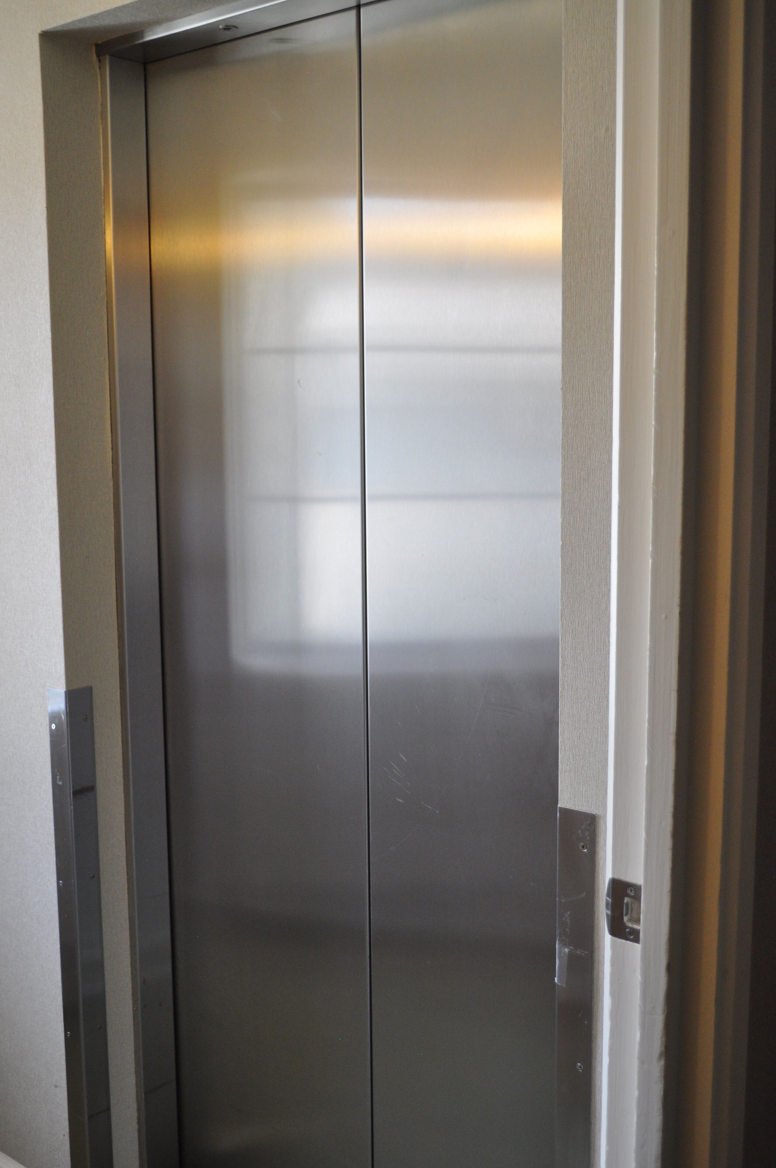 Une porte d’ascenseur métallique, dotée d’une surface réfléchissante et d’une poignée bien visible.