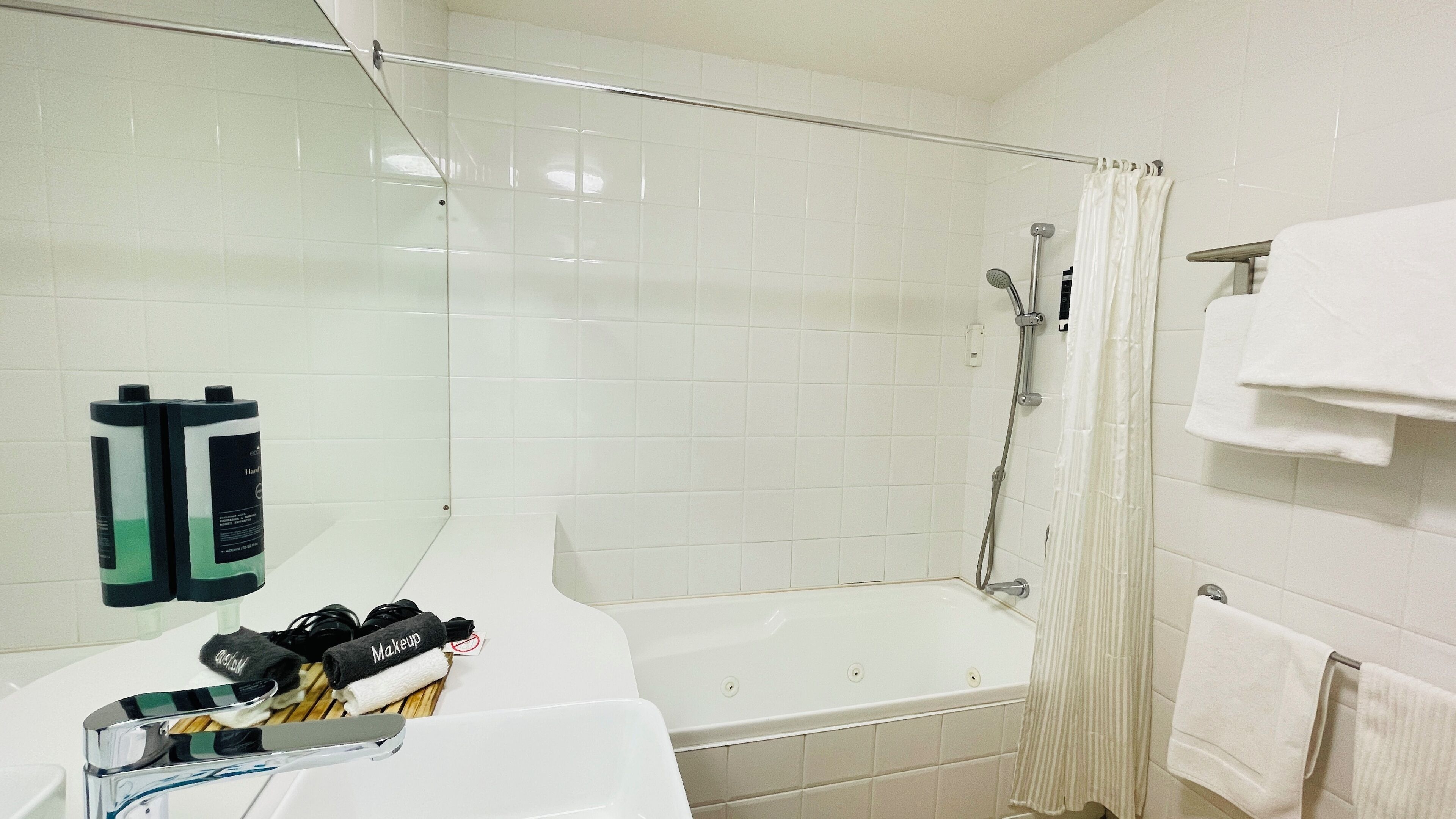 Une salle de bain avec une baignoire, une douche et des toilettes. On y trouve deux bouteilles de shampoing et un porte-serviettes avec des serviettes.