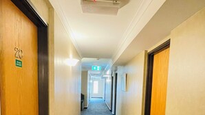 A hotel hallway with carpeted floors, wooden doors, and a ceiling light fixture. - City Suites Tauranga (Tauranga)