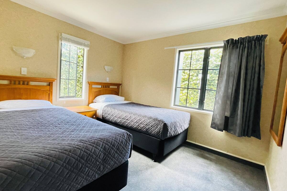 Una habitación de hotel con dos camas, una ventana con cortinas y un cabecero de madera.