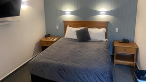 A hotel room with a bed, two bedside tables, a TV mounted on the wall, and an air conditioning unit. - City Suites Tauranga (Tauranga)