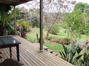 A wooden deck with a glass table and chairs, overlooking a well-maintained garden with various plants and trees. - Wharepuke Subtropical Accommodation (Kerikeri)