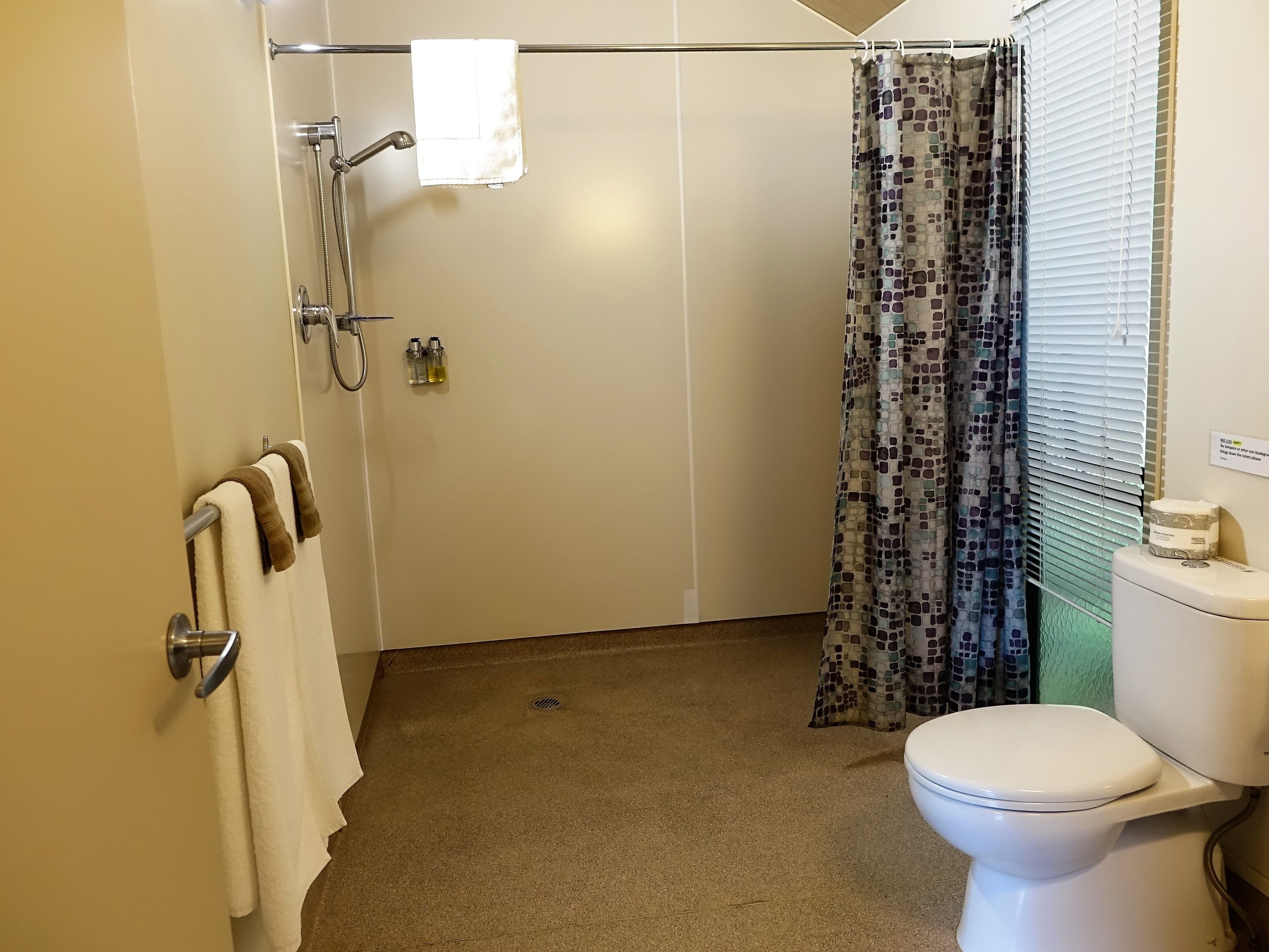 Et badeværelse med bruser, toilet og håndklædestativ.