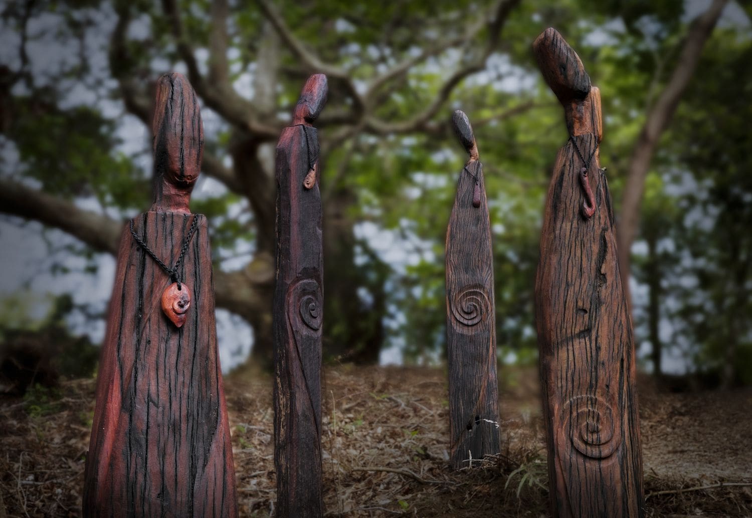 Quatre sculptures en bois ornées de motifs en spirale, installées dans un cadre naturel en plein air.