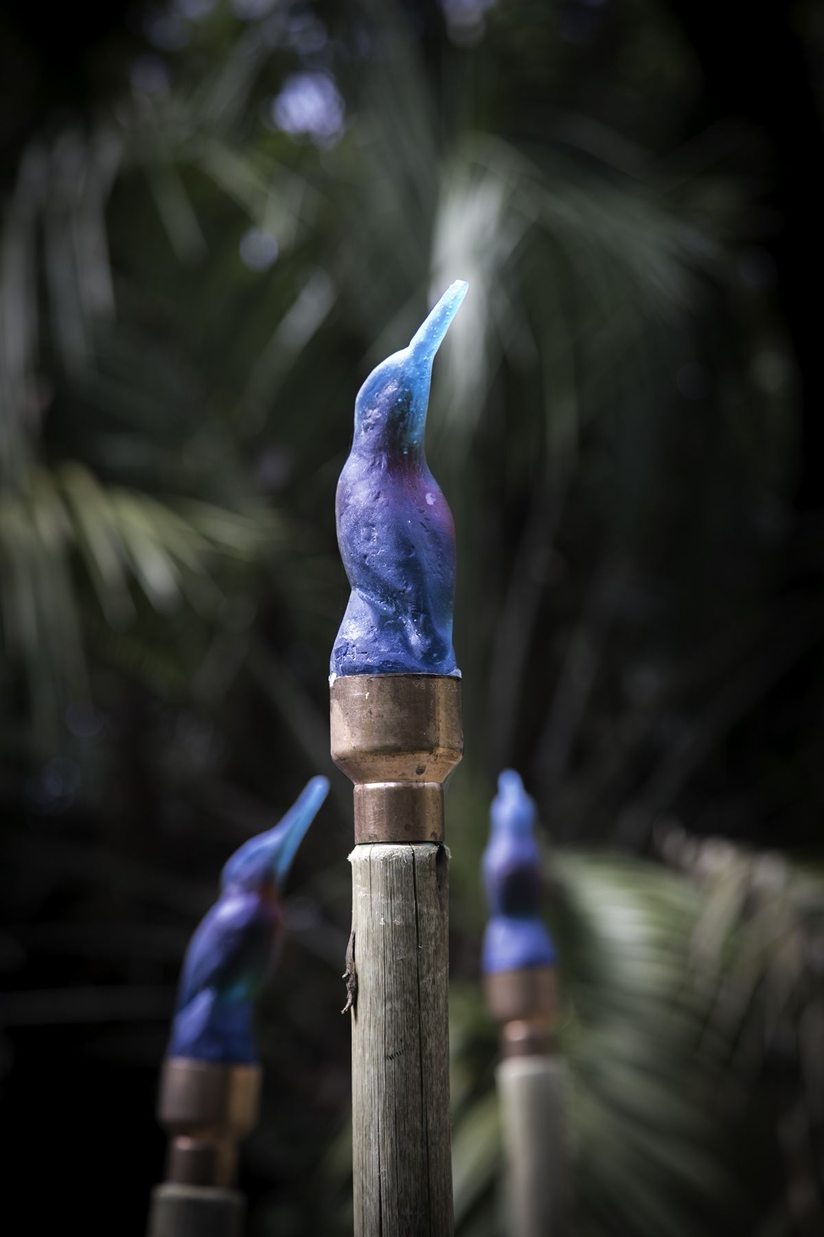 A close-up of a blue, bird-shaped object on a wooden post.