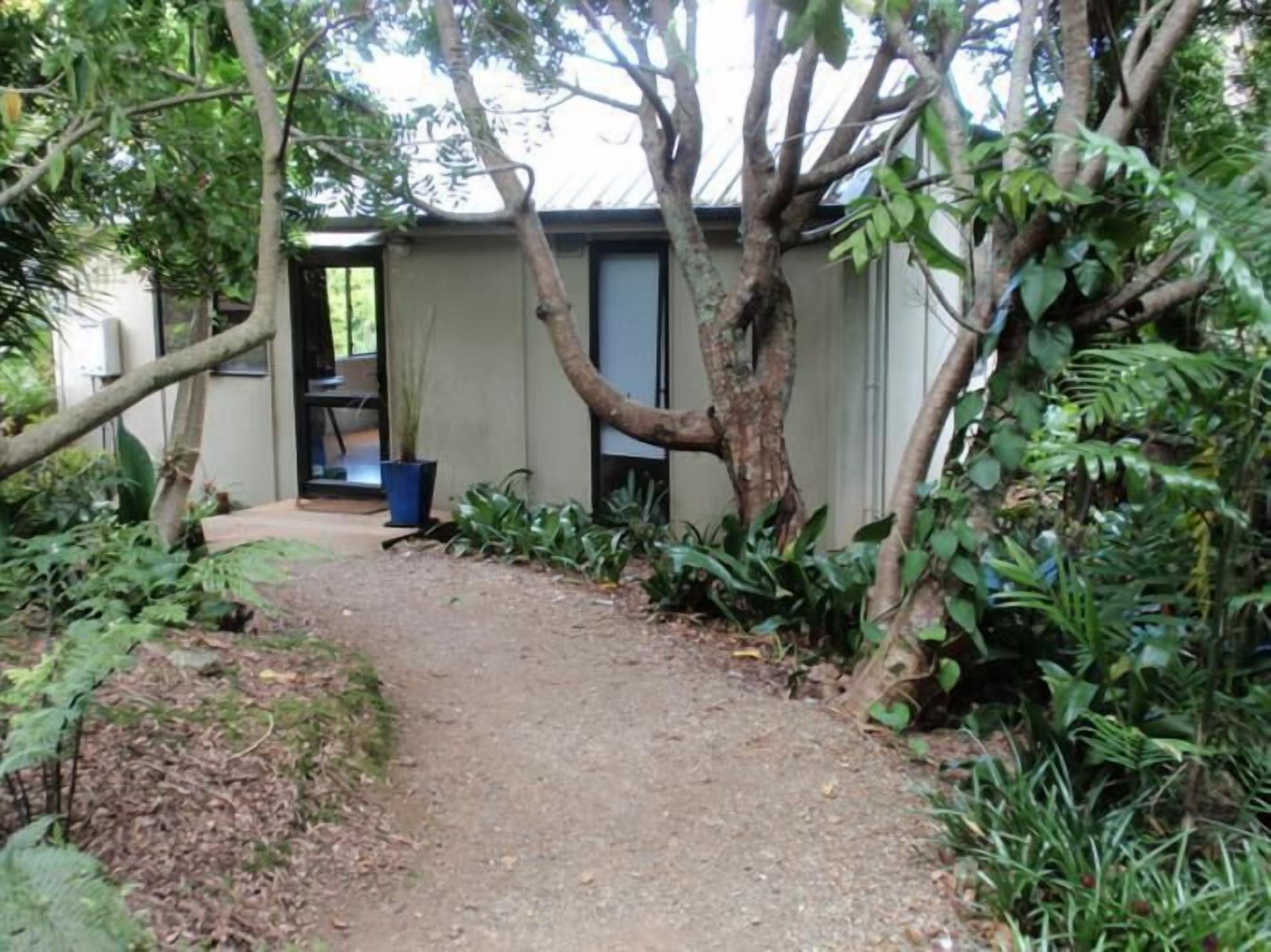 A pathway leading to a small, single-story building surrounded by dense vegetation.