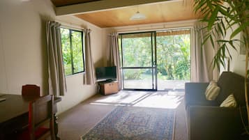 A room with a television on a wooden cabinet, a sofa, a dining table, and a large window with curtains.