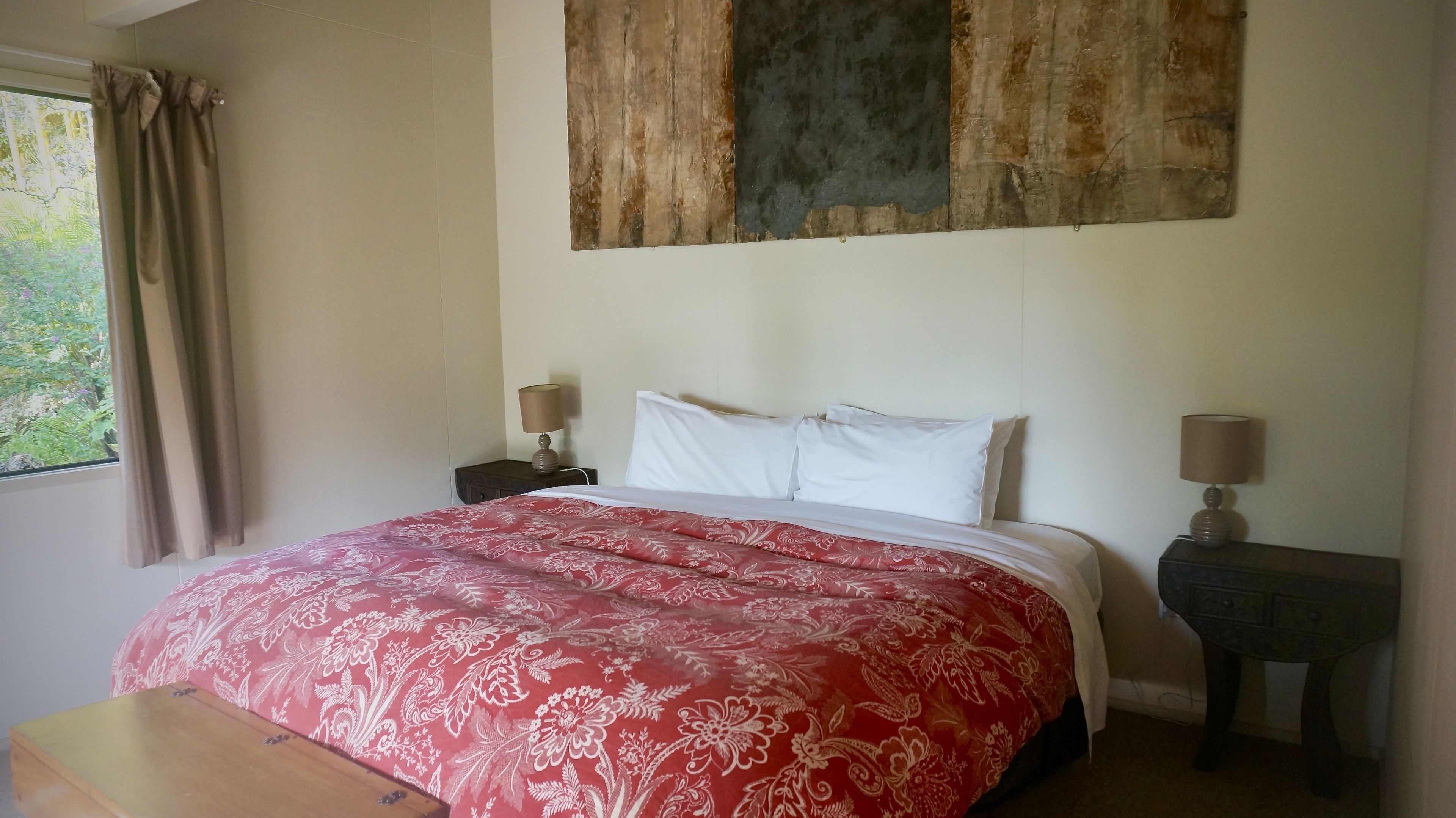 Un dormitorio con una cama grande, dos mesitas de noche con lámparas, una ventana con cortinas y una obra de arte de madera sobre la cama.