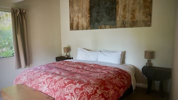 Un dormitorio con una cama grande, dos mesitas de noche con lámparas, una ventana con cortinas y una obra de arte de madera sobre la cama.