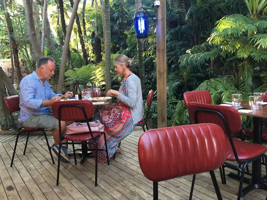 Una terraza de madera con sillas rojas y una mesa dispuesta para dos, rodeada de abundante vegetación.