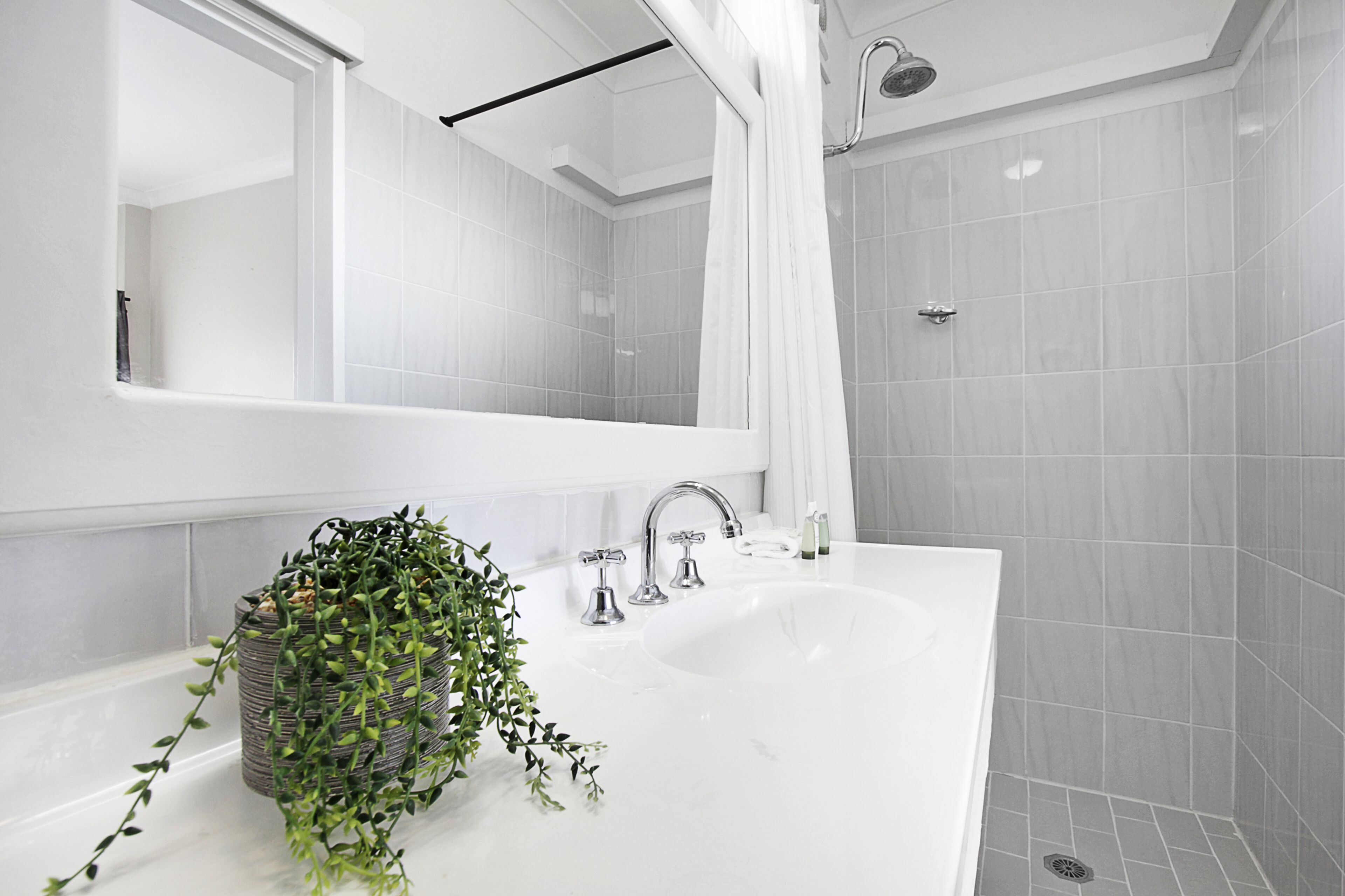 A modern bathroom with a white sink, a large mirror, and a shower area.