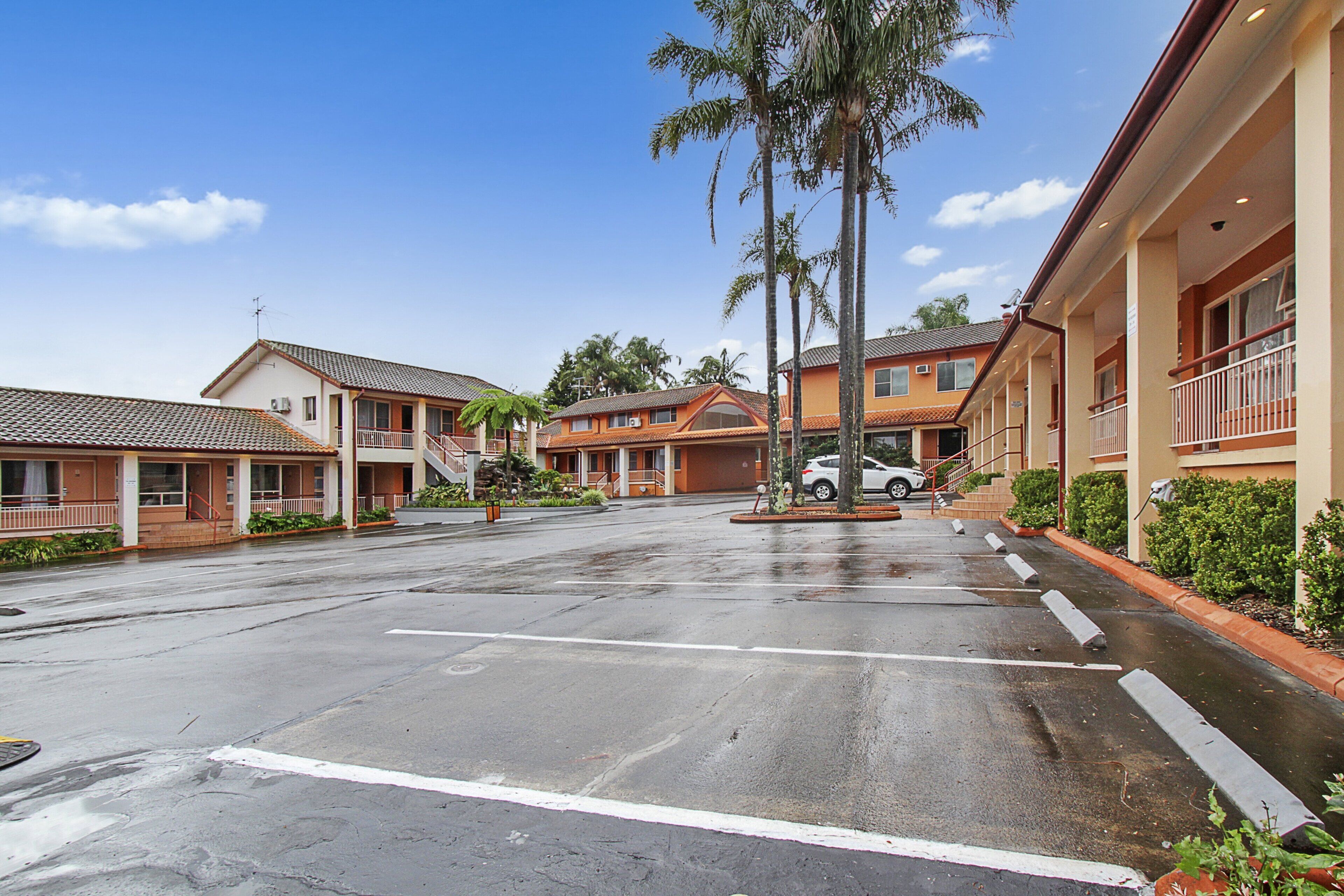 A hotel with a parking lot, multiple buildings, and palm trees.