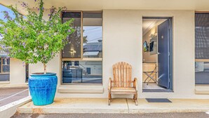 Un edificio con una maceta azul grande que tiene un árbol, una silla de madera y una puerta que da a un espacio interior.