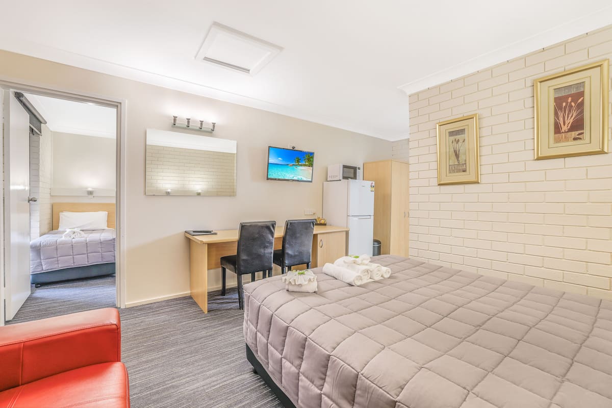 A hotel room with a bed, a desk, two chairs, a television, and a refrigerator.