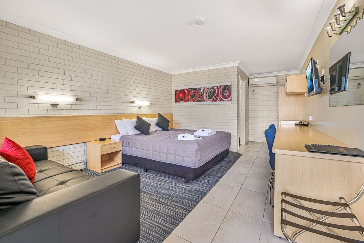 A modern hotel room with a bed, a sofa, a desk, and a TV.