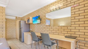 Cocina compacta con refrigerador, microondas y lavamanos. Hay un comedor con dos sillas y una mesa. Se observa un letrero de 'No Fumar' en la pared.