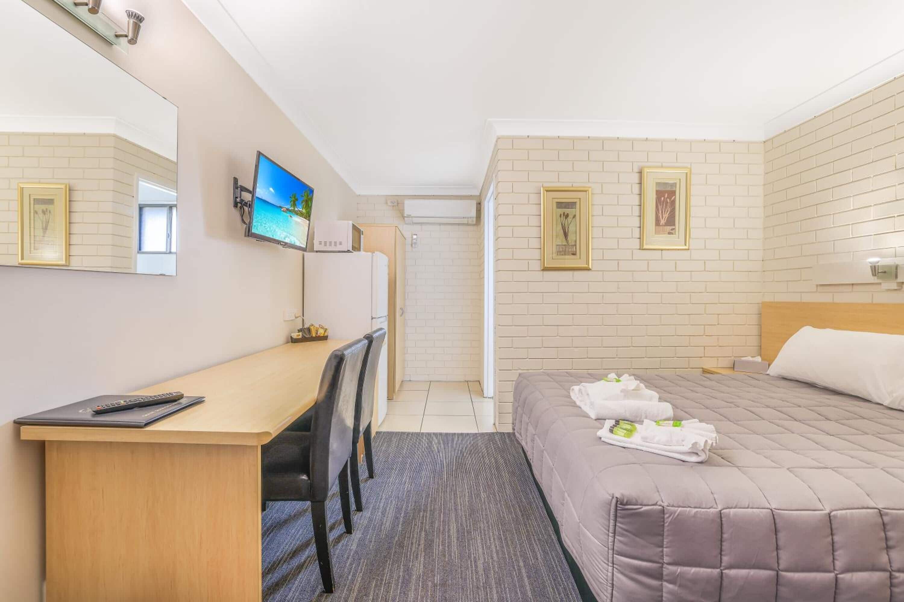 A hotel room with a bed, a desk with a chair, a television, and a mirror.
