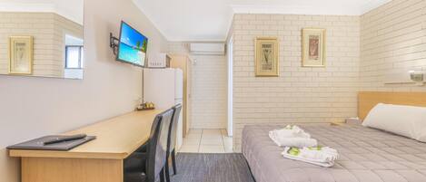 Una habitación de hotel con una cama, un escritorio con una silla, un televisor y un espejo.
