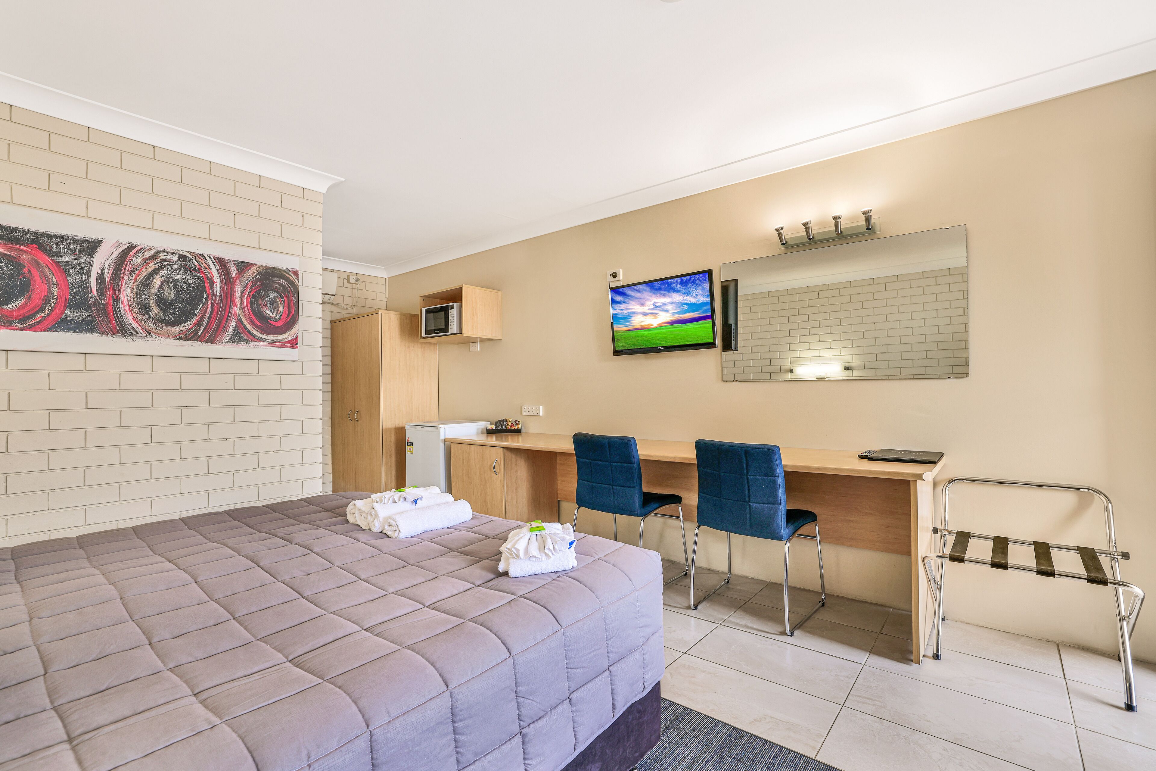 Habitación de hotel con cama, escritorio, dos sillas, televisión, microondas y espejo de baño.