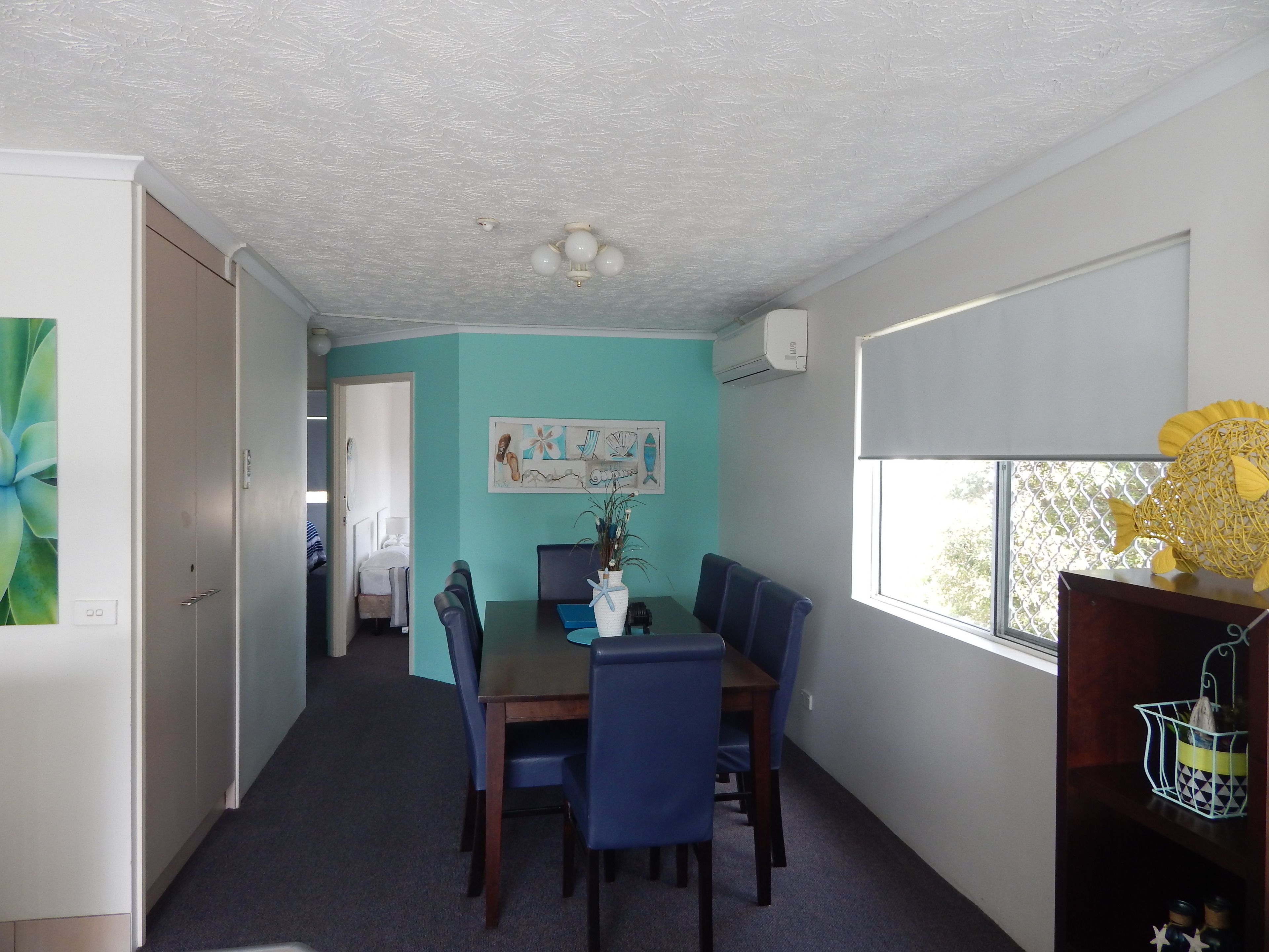 A dining area with a table and chairs, a painting on the wall, and a window with a view.