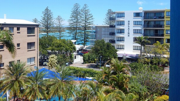 Un hotel con varios pisos, balcones y una zona de piscina con sombrillas.